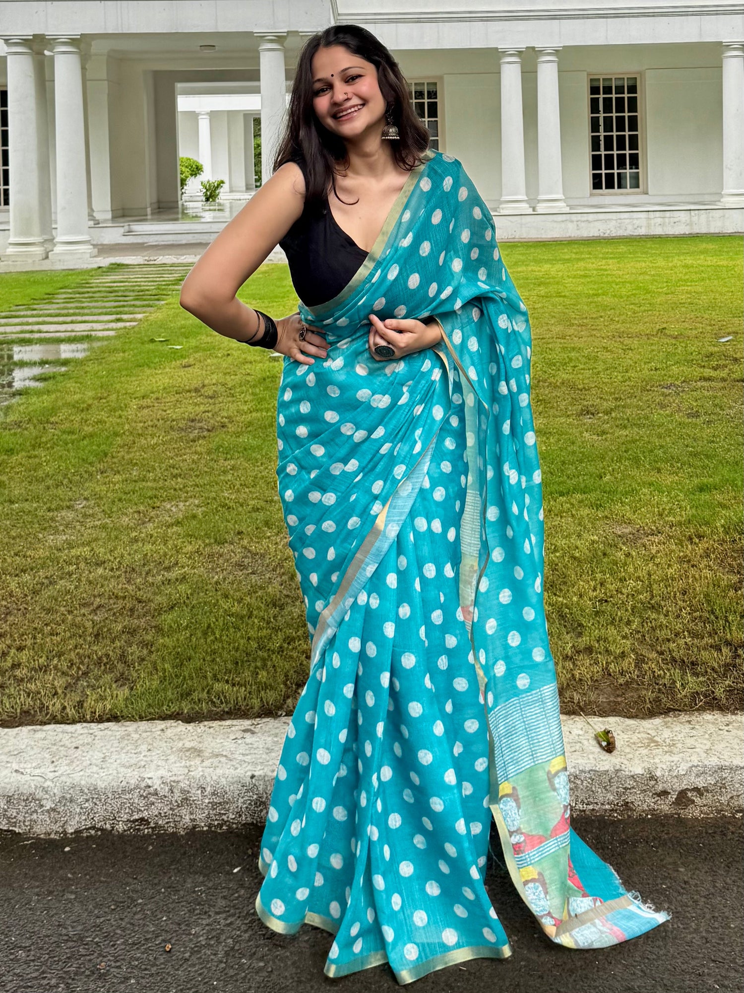 An image of woman wearing a dusky brown linen saree and is standing sideways with her pallu stretched towards the front. 