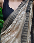 Person wearing a black top with a beige and brown patterned scarf draped over their shoulder.