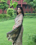 Woman in a saree standing in a garden with green grass and trees.