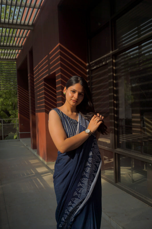 A woman standing on a balcony wearing a blue saree with a fish print and premium pure cotton lace on the pallu.