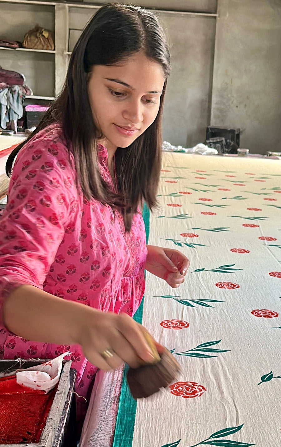 Woman in pink dress working on a floral fabric in a room with a window.