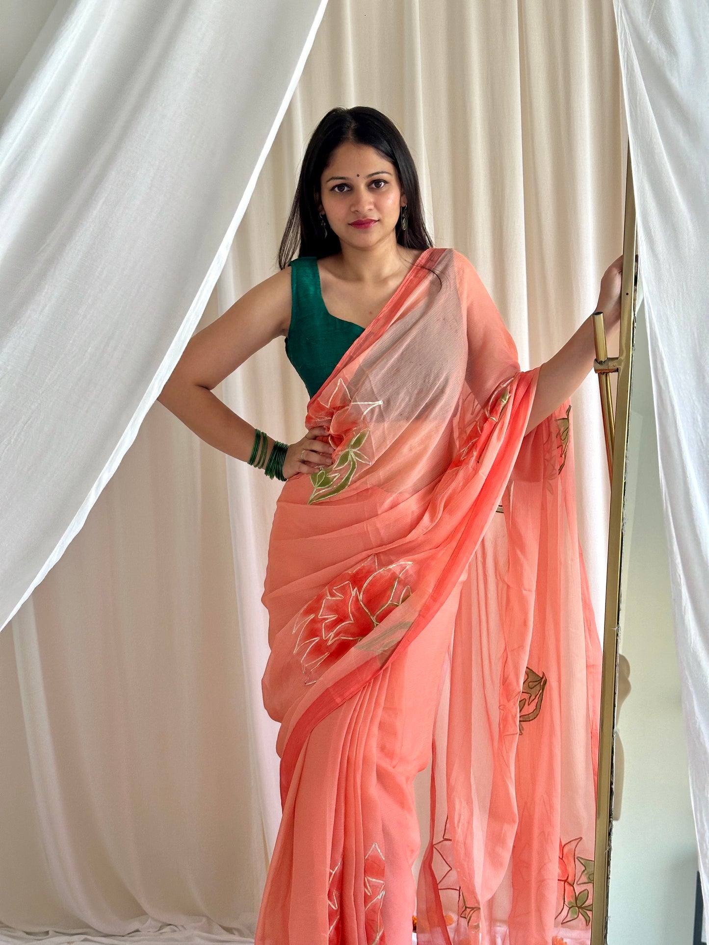 Woman wearing a peach saree with floral patterns against a white curtain background