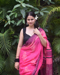 Woman in a pink and black saree standing in front of green foliage