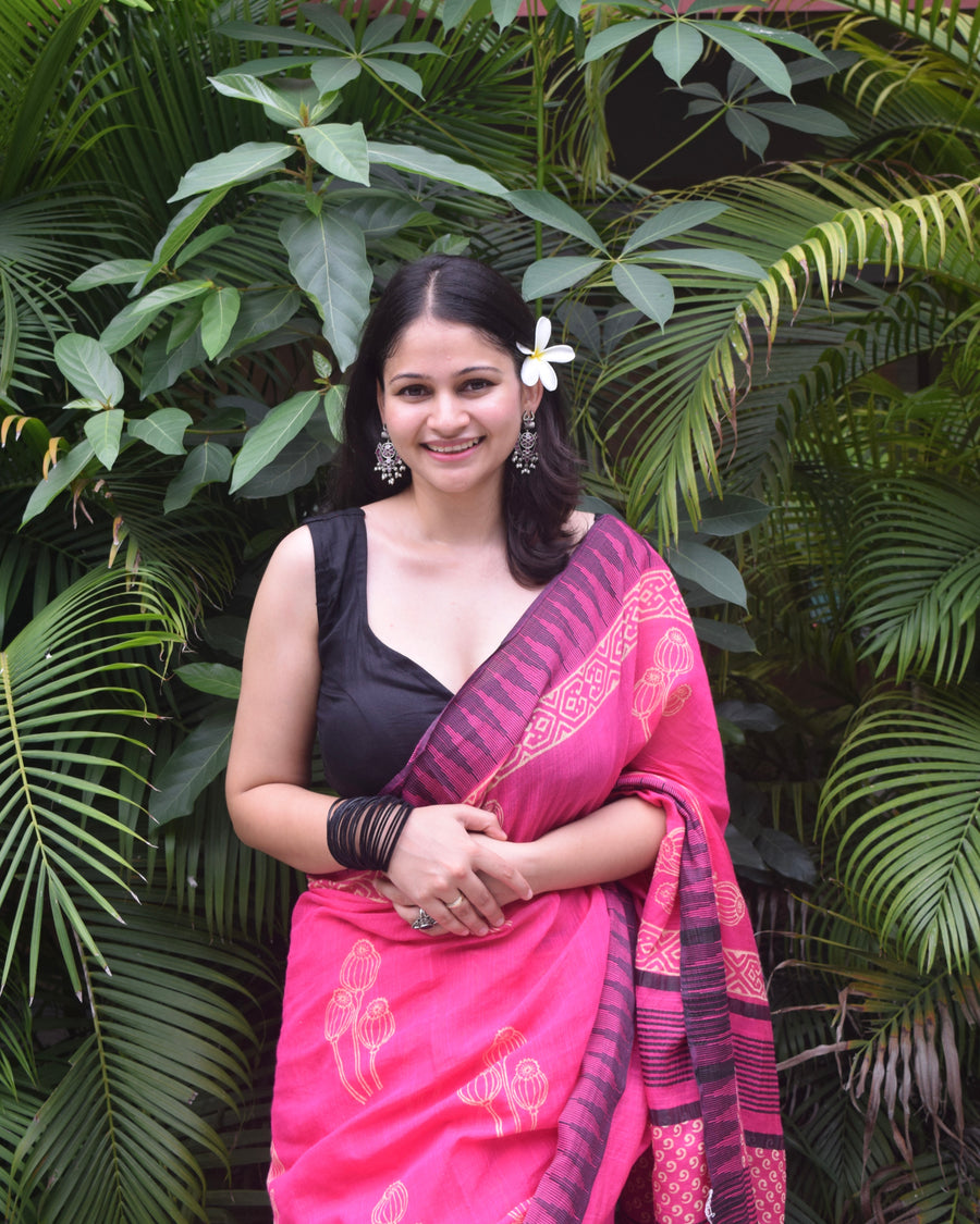 Woman in a pink saree with a black blouse standing among green plants
