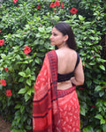 Woman wearing a red saree with a black blouse against a green leafy background