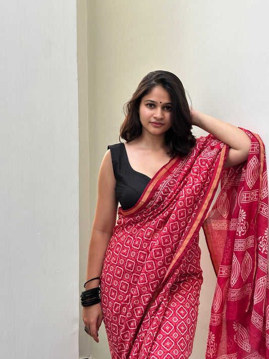 Woman wearing a red patterned saree with a black blouse against a plain background