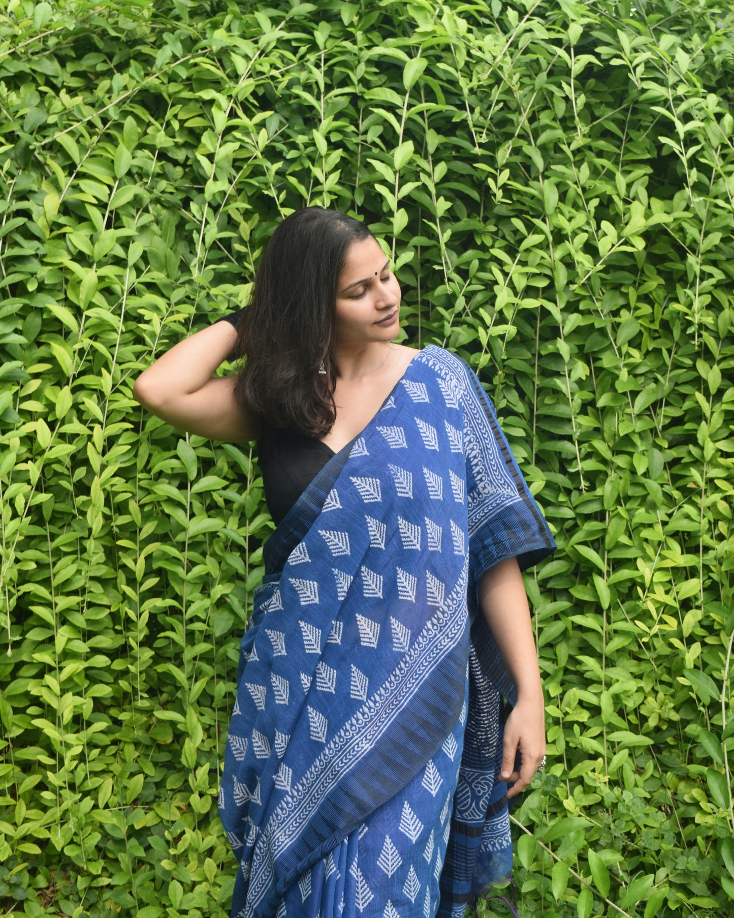 Woman wearing a blue saree with a black blouse against a green leafy background