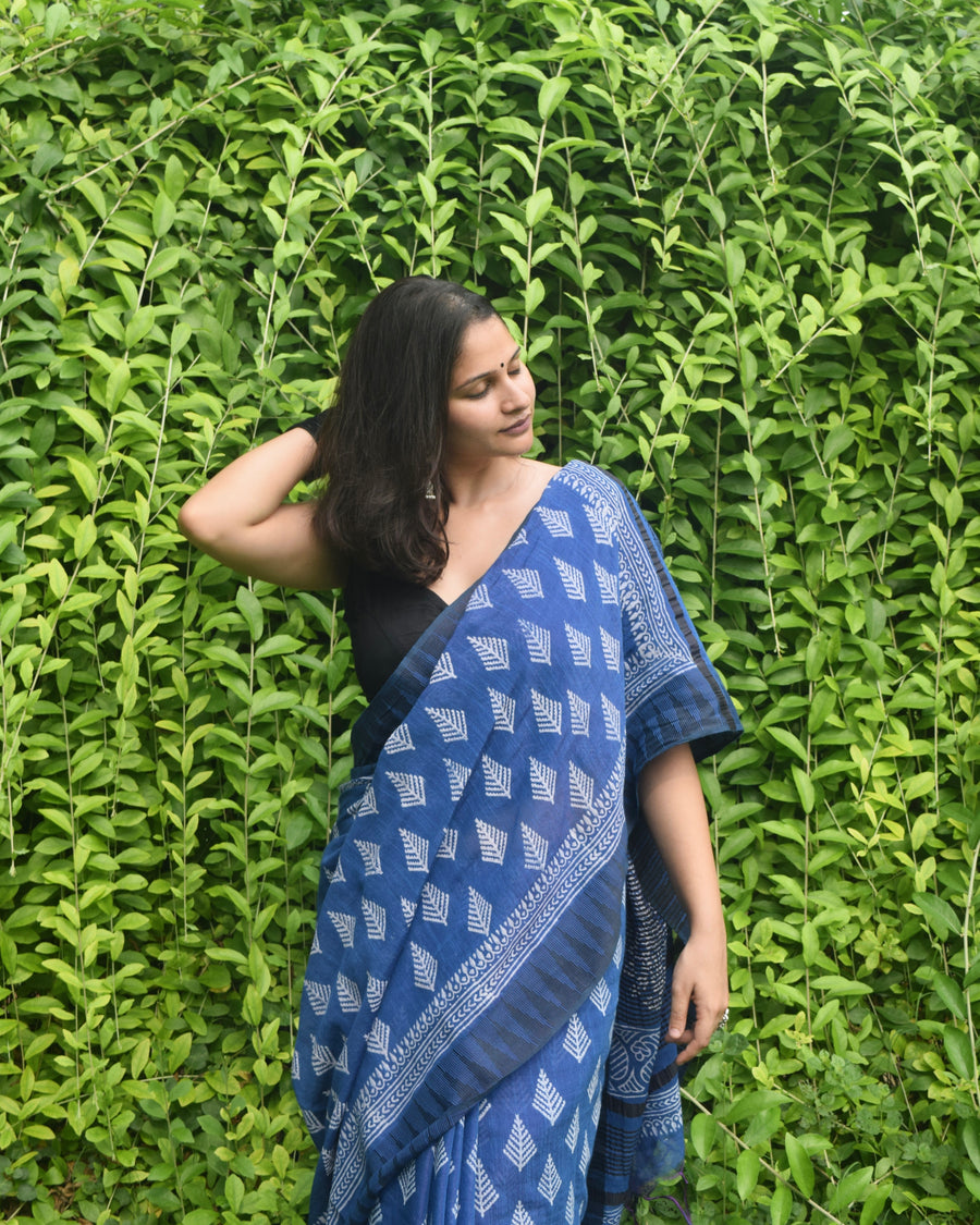 Woman wearing a blue saree with a black blouse against a green leafy background